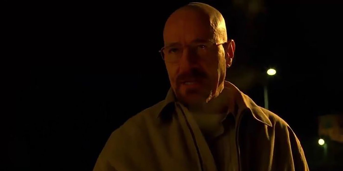 Walter White at night standing on the street in Breaking Bad standing in the dark, looking uo at someone with a scary look on his face.