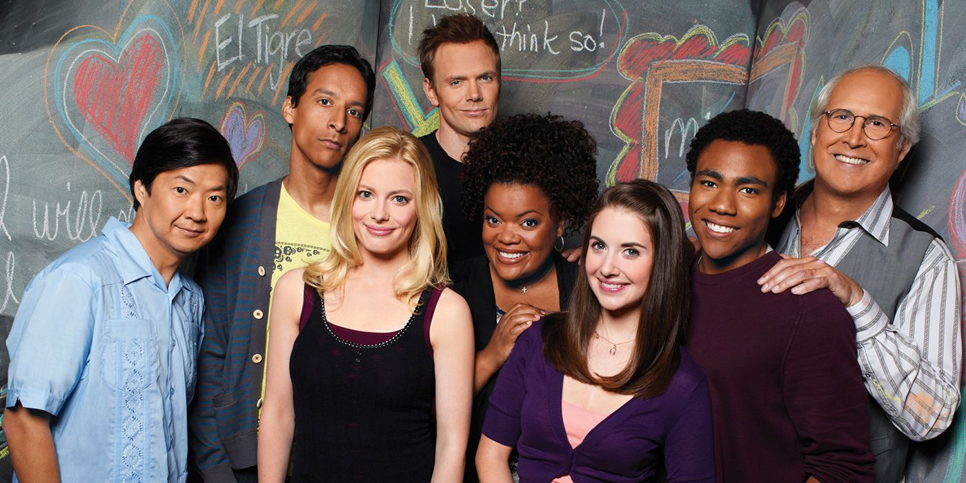 The cast of Community posing for a cast photo in front of a wall with chalk drawings on it