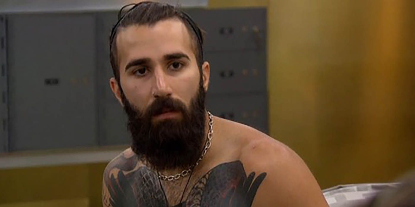 Paul from Big Brother looking at someone, no shirt on and with a beard.