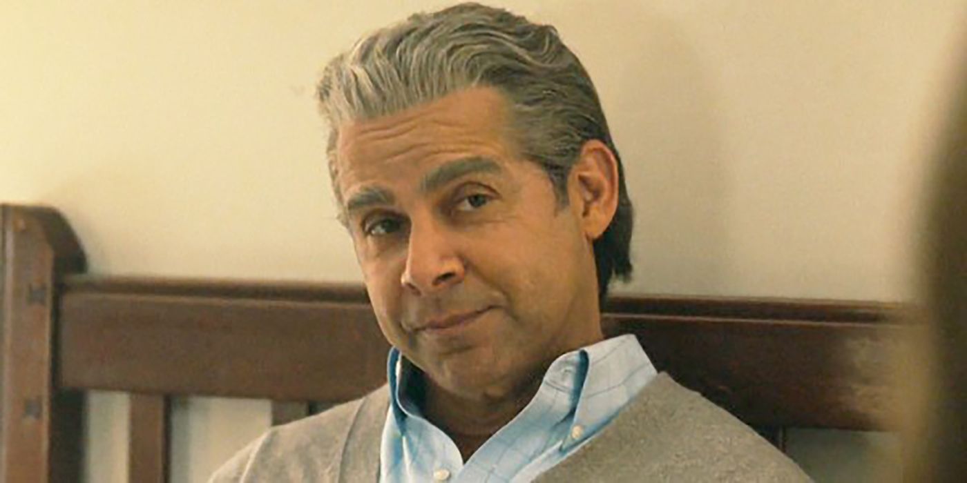Miguel in This Is Us sitting on a bed, smiling with grey hair.