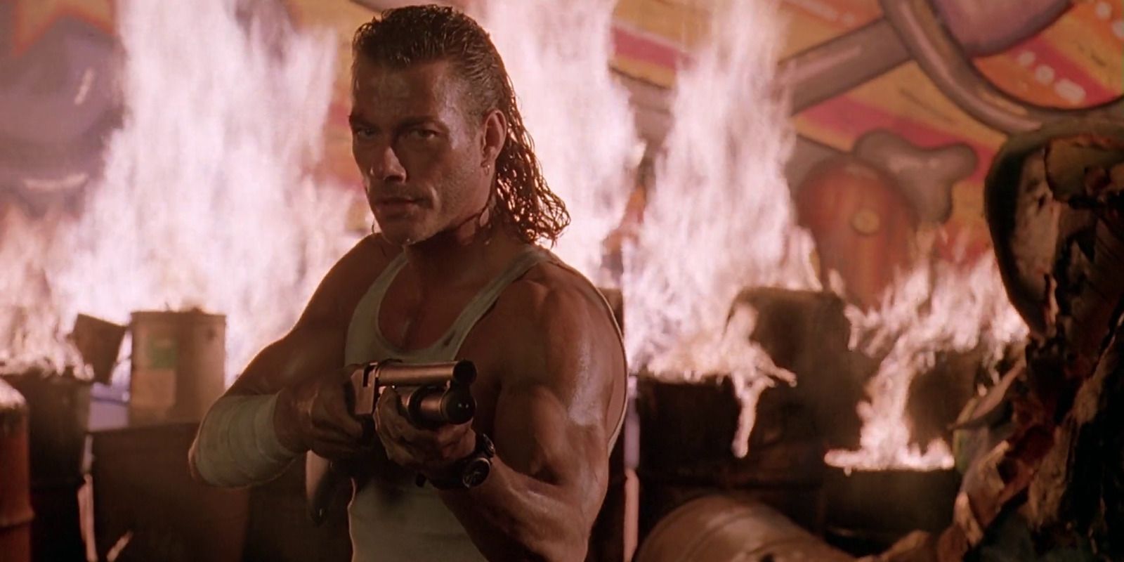 Image of Jean-Claude Van Damme as Chance Bordeaux in Hard Target Chance is wearing a vest and pointing a pump-action shotgun toward the right of the camera.