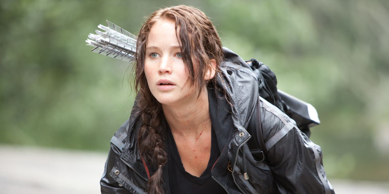 Katniss crouching and looking to the distance in The Hunger Games.