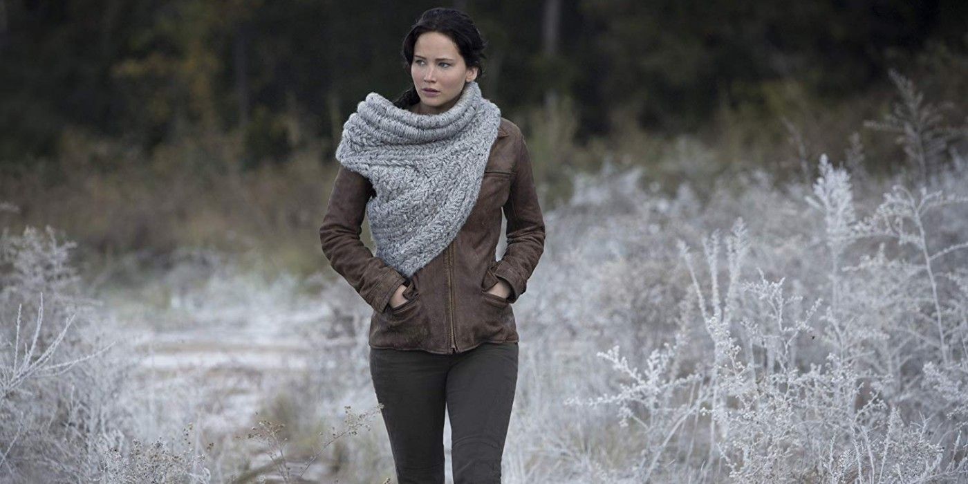 Katniss Everdeen walks through snow covered grass in a jacket in The Hunger Games Catching Fire.