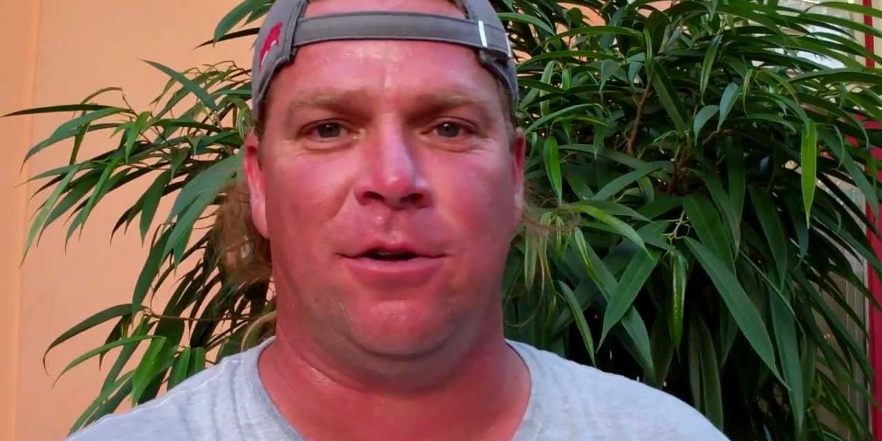 Chris Daugherty from Survivor standing with a backwards hat and a tree behind him.