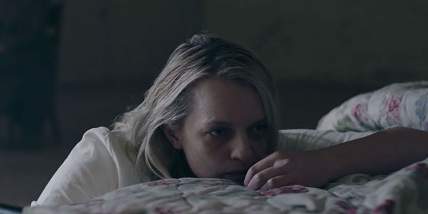 June with her chin resting on a bed in a scene from The Handmaid's Tale