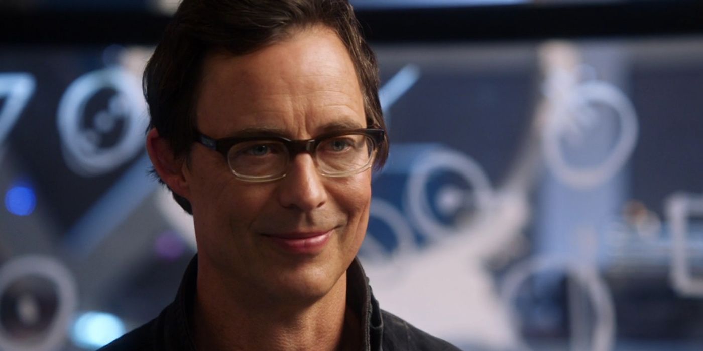 Head shot of Harry Wells wearing glasses, standing at Star Labs, softly smiling