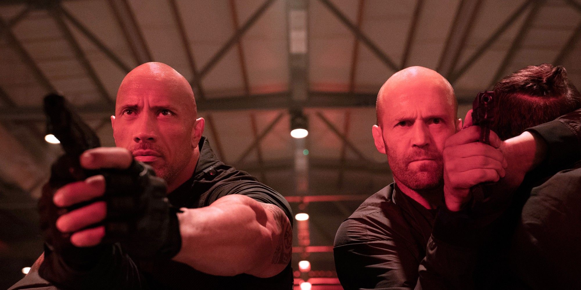 Jason Statham as Shaw and Dwayne The Rock Johnson as Hobbs pointing guns in a warehouse in Hobbs & Shaw