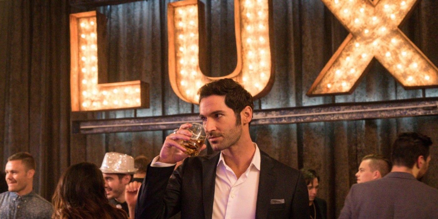 Lucifer standing at LUX, drink in hand with the lit-up bar sign behind him.