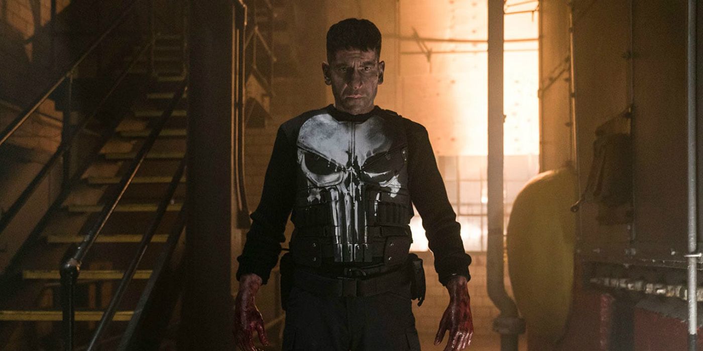 Jon Bernthal wearing a bulletproof vest with a skull on it and looking troubled in Punisher