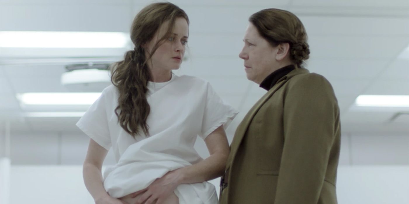 Ofglen em um vestido branco de hospital segurando seu estômago, tia Lydia olhando em uma cena de The Handmaid's Tale