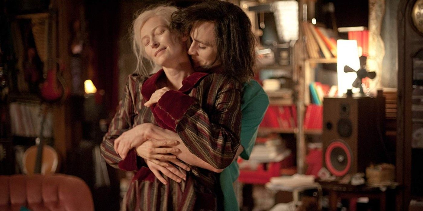 Tom Hiddleston in a green shirt hugging Tilda Swinton who's wearing striped pyjamas in Only Lovers Left Alive