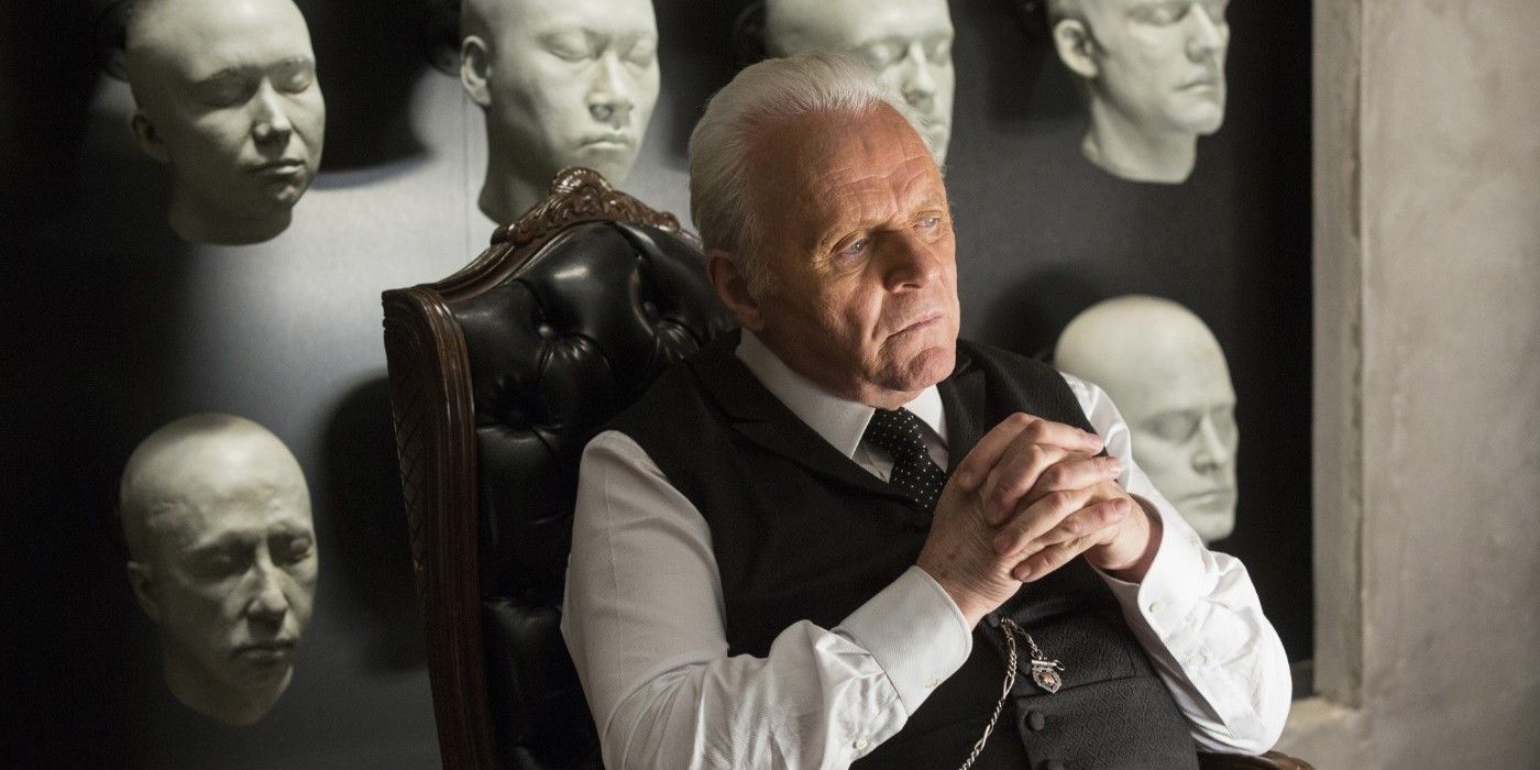 Anthony Hopkins as Dr. Robert Ford sitting in front of host heads mounted on a wall in Westworld