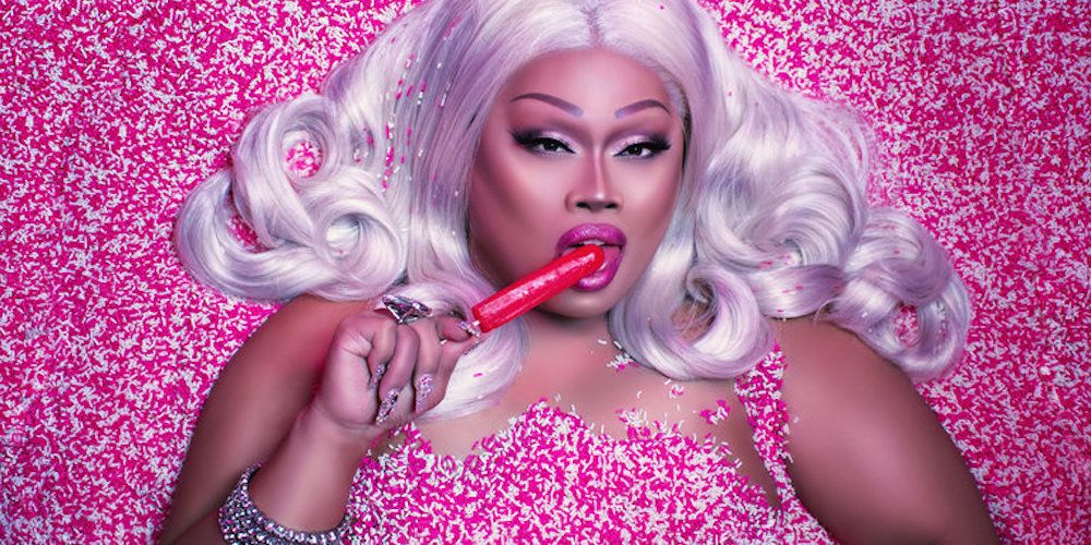 Jiggly Caliente lies on a bed on pink sprinkles and licks a lollipop
