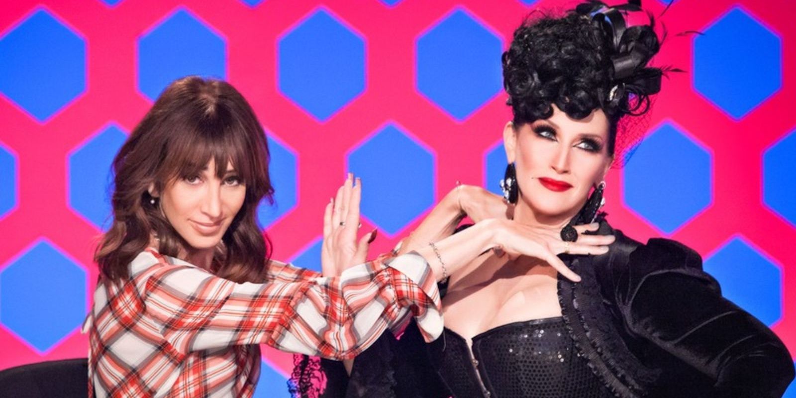 Merle Ginsberg and Michelle Visage pose together behind the judges table on RuPaul's Drag Race