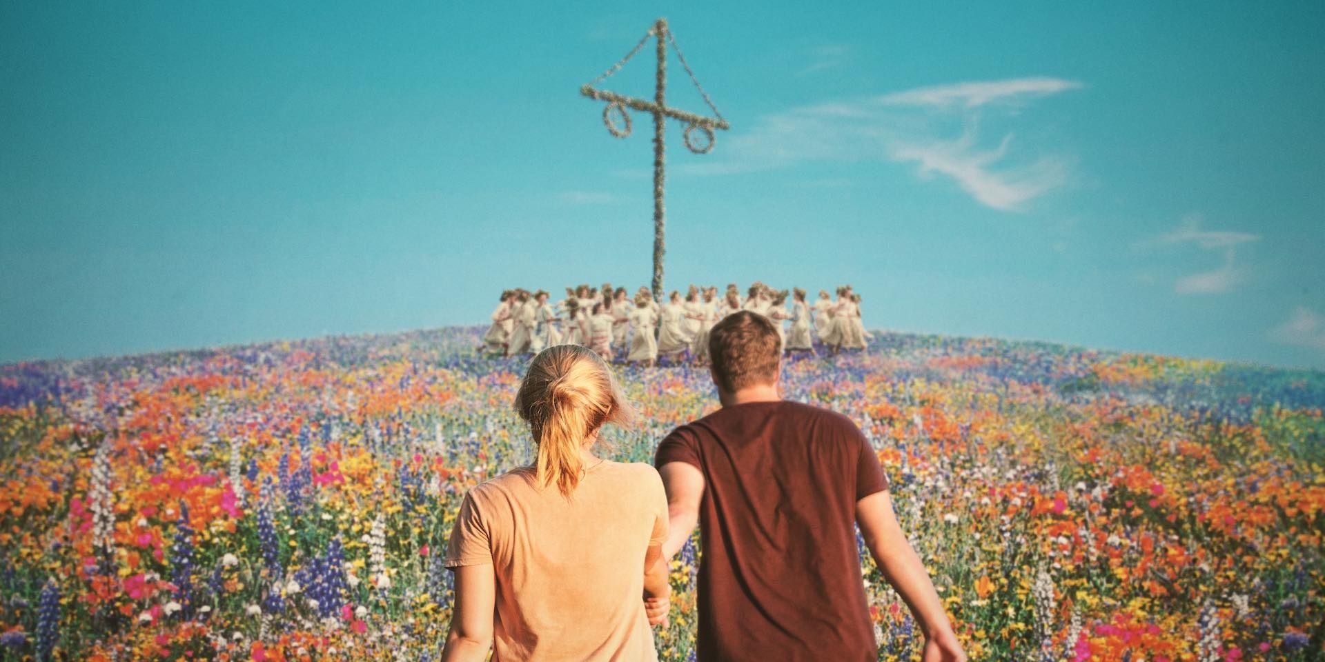 Two people walking to a maypole across a field of flowers.