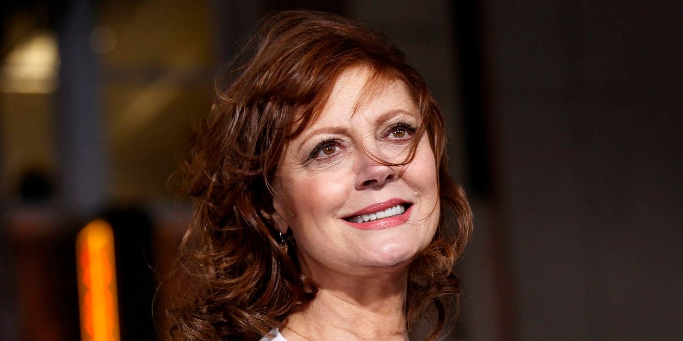 Susan Sarandon smiles, looking upward with hair in her face.