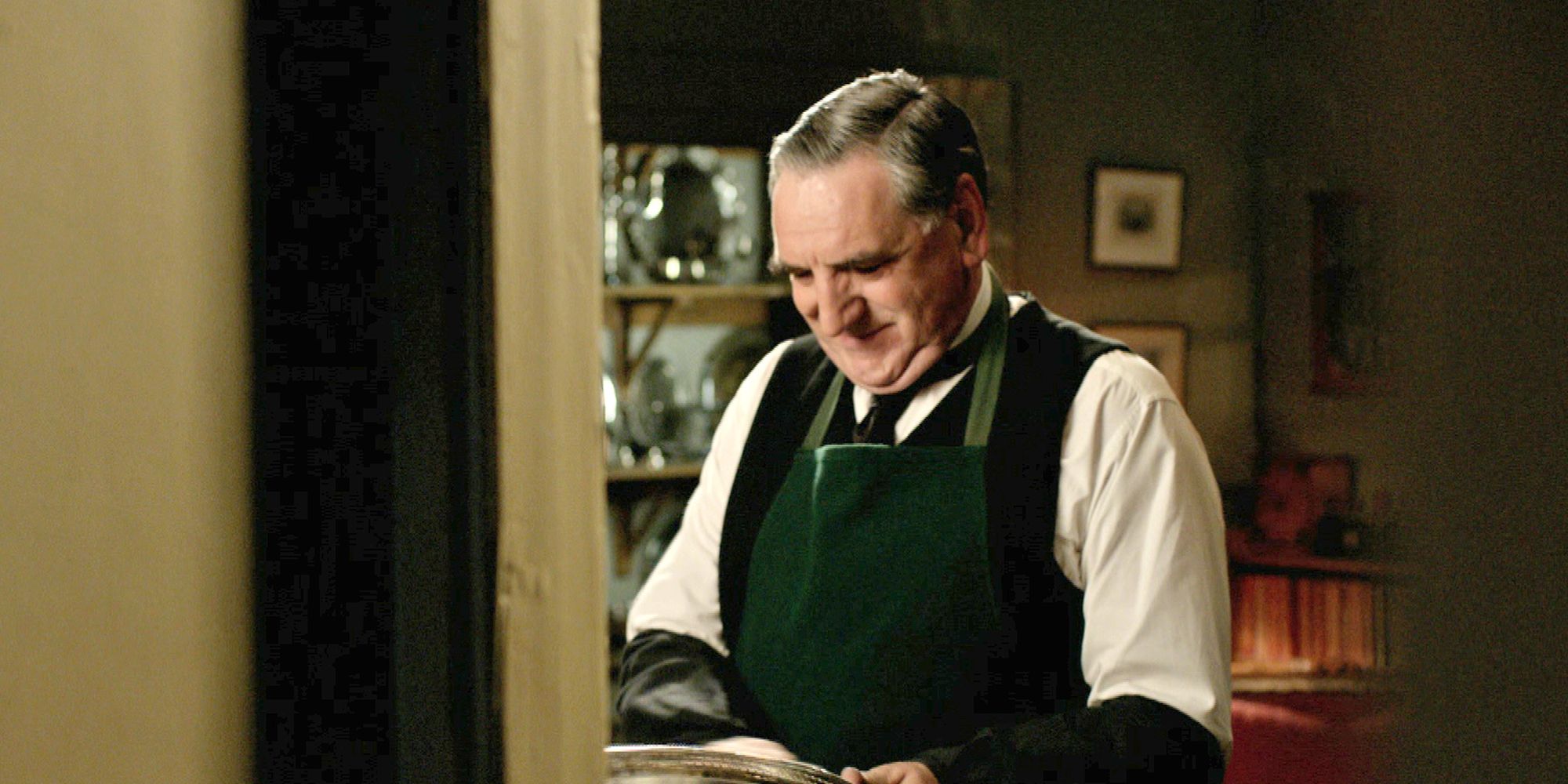 Charles Carson smiling while looking down at something in Downton Abbey