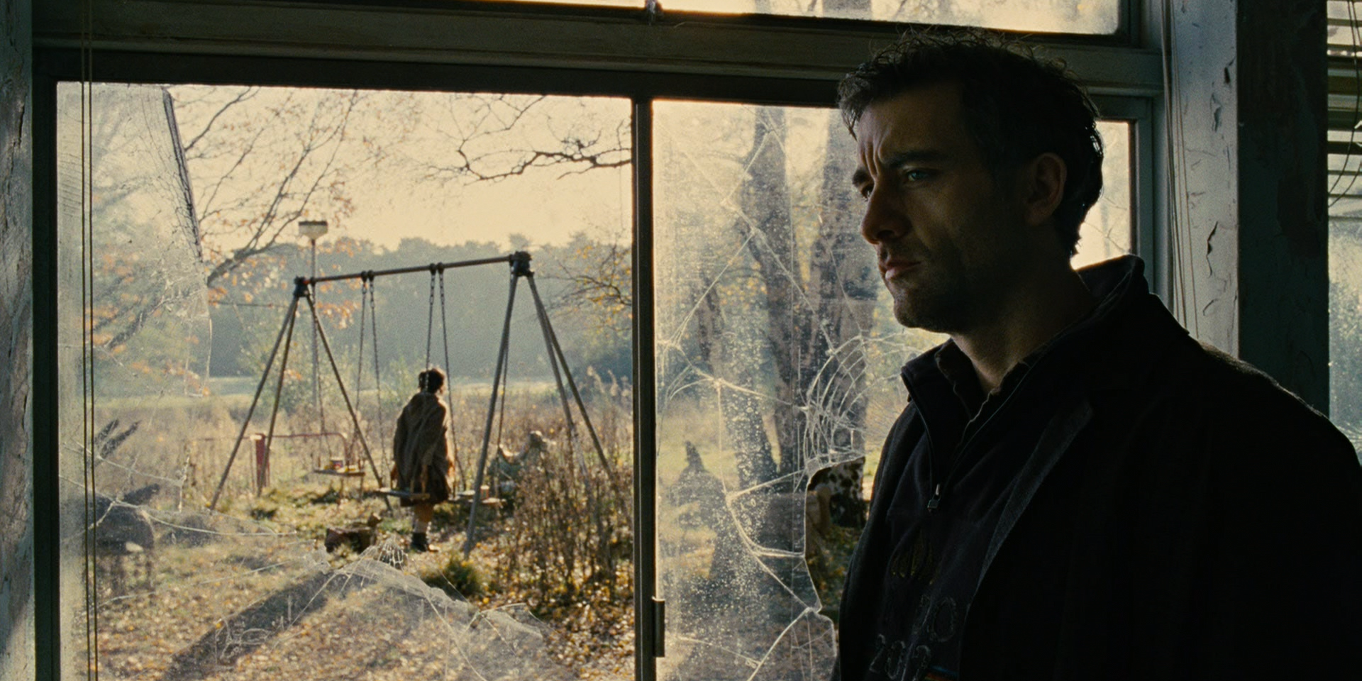 Theo standing beside a broken window with a desolate scene outside in Children of Men