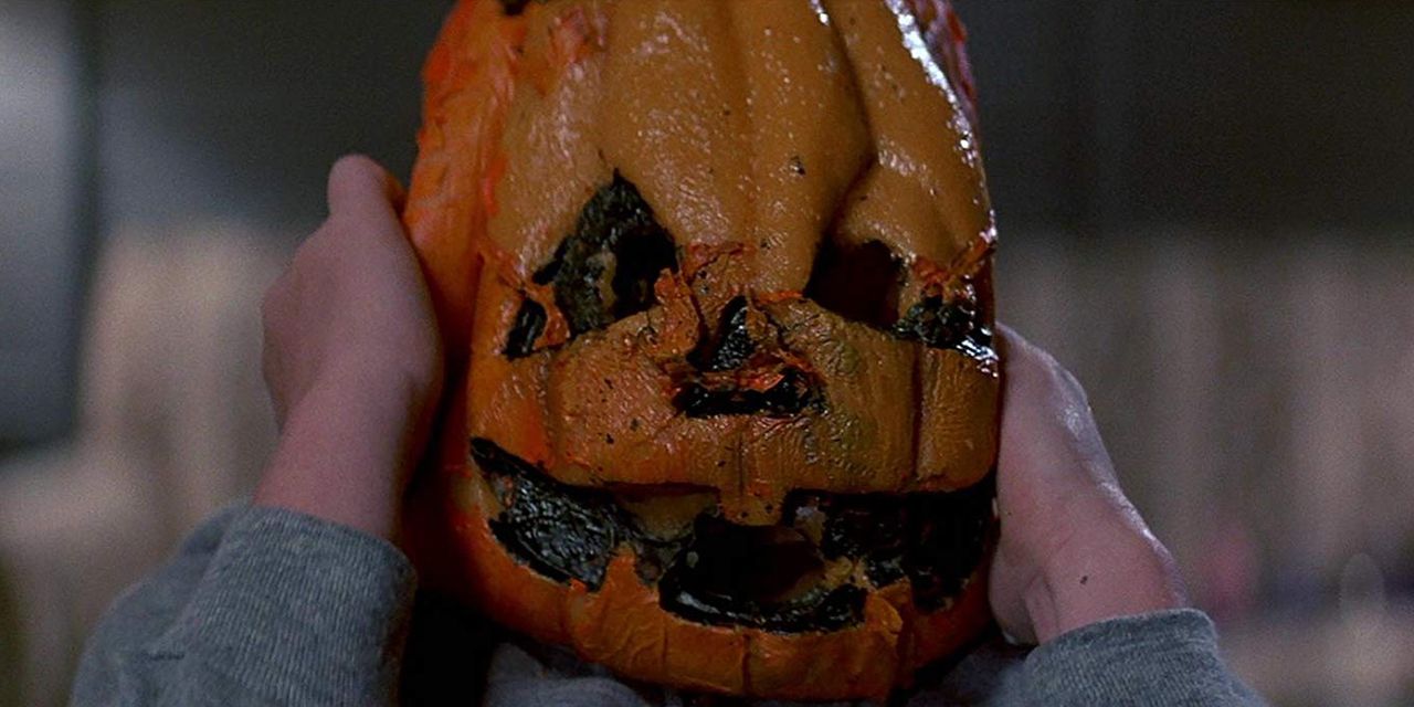 A child clutching at the sides of the jack o lantern mask it's wearing in Halloween III Season of the Witch