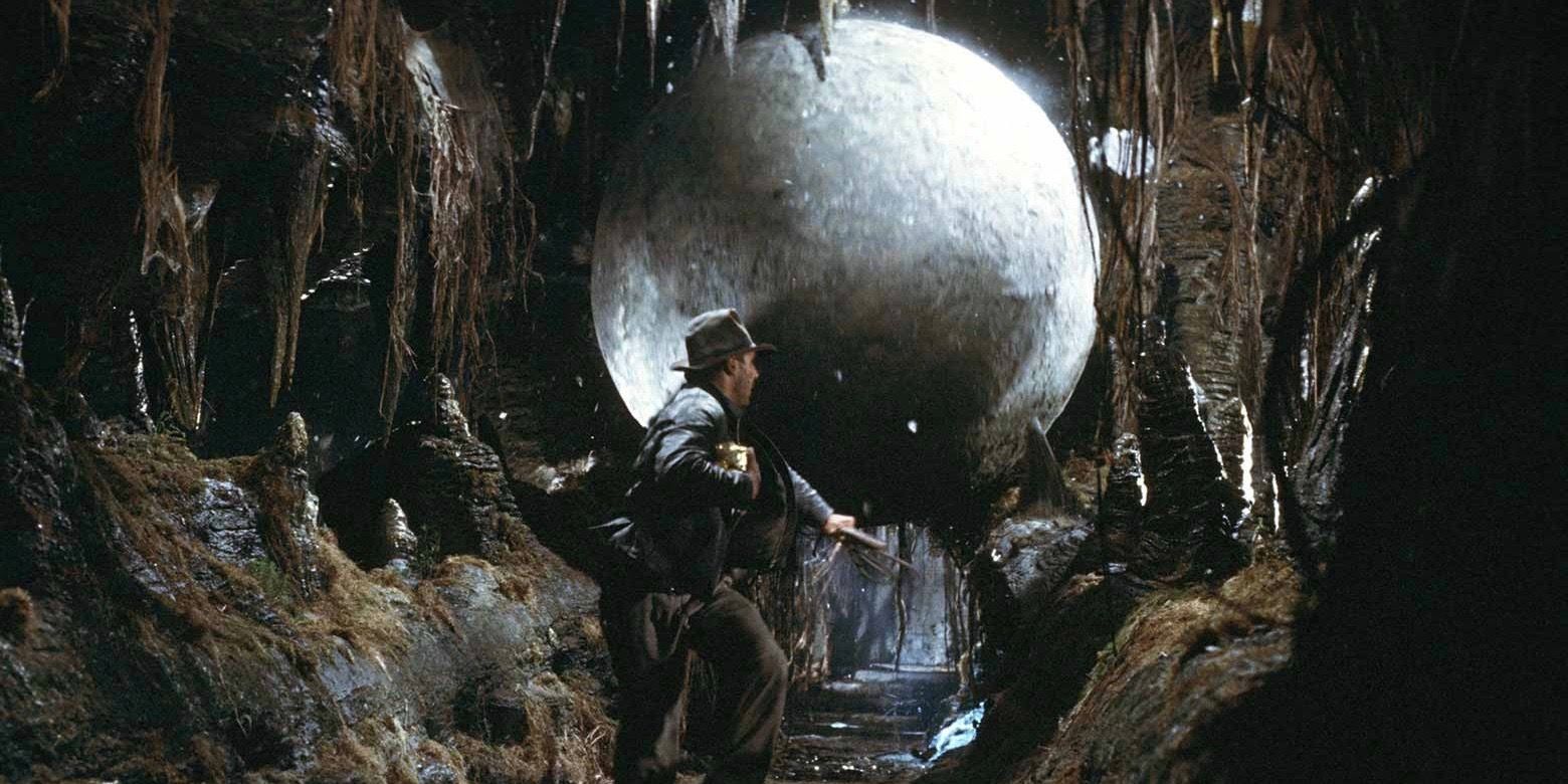 Harrison Ford como Indiana Jones sendo perseguido por uma pedra em Os Caçadores da Arca Perdida