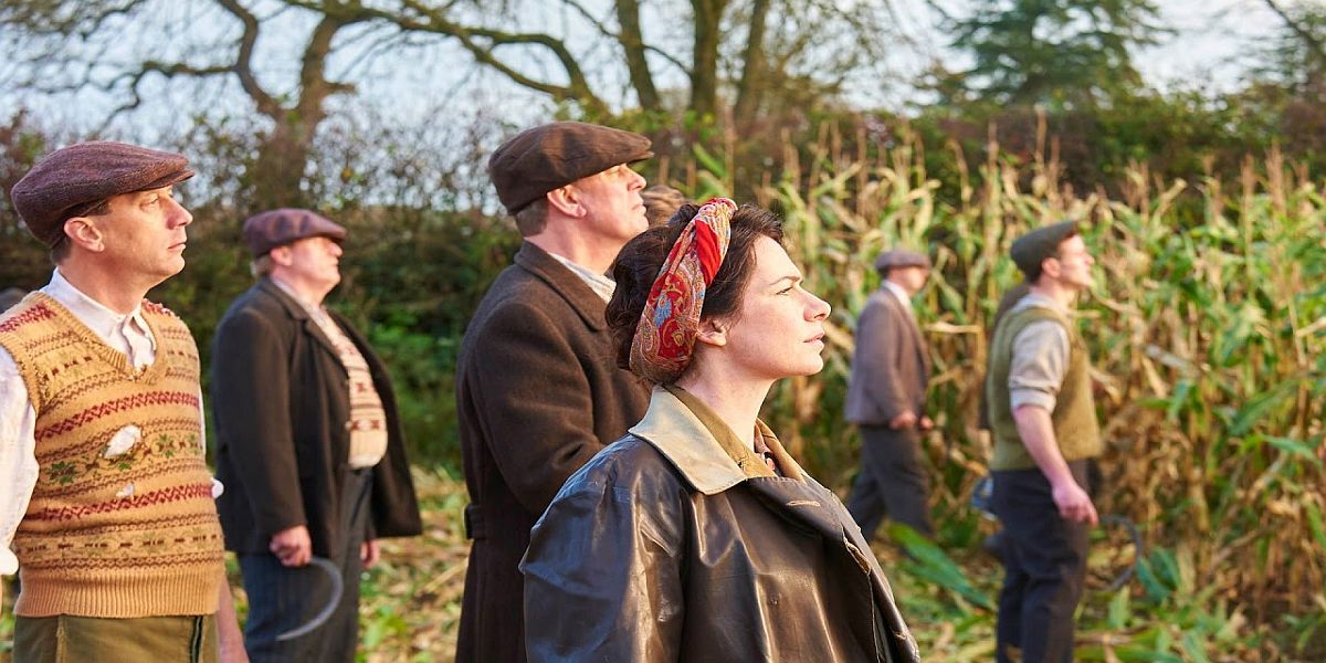 A group looks up at the sky on the edge of a field in Home Fires