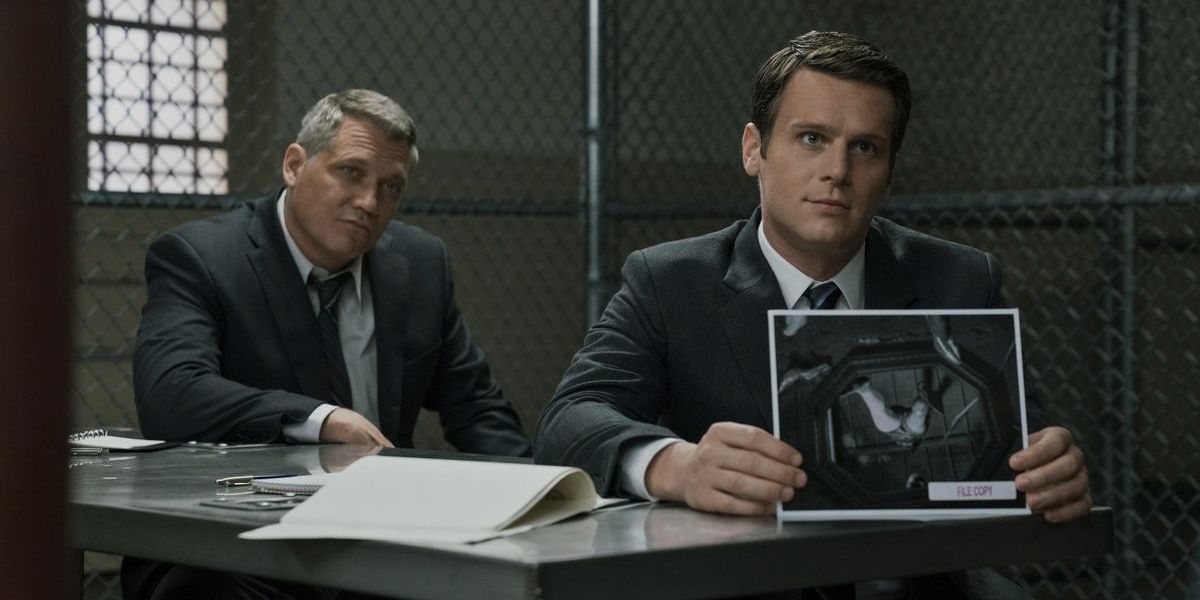 Holden holds an image of a crime scene while Bill looks on in a still from Mindhunter