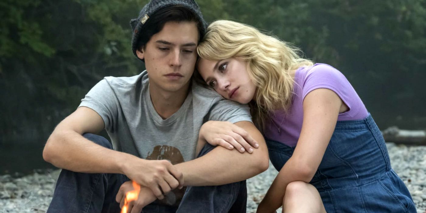 Betty resting her head on Jughead's shoulder by a campfire in Riverdale