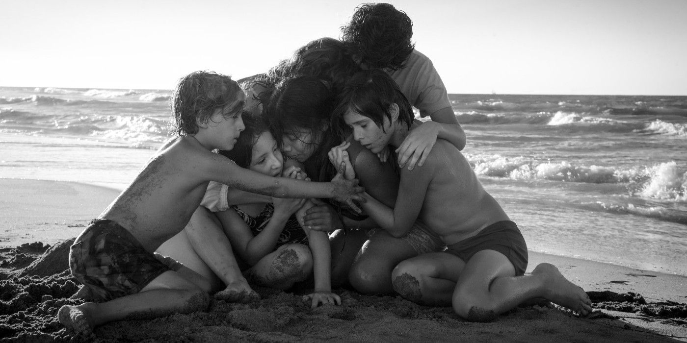 A group of children embraces a woman at a beach in Roma.