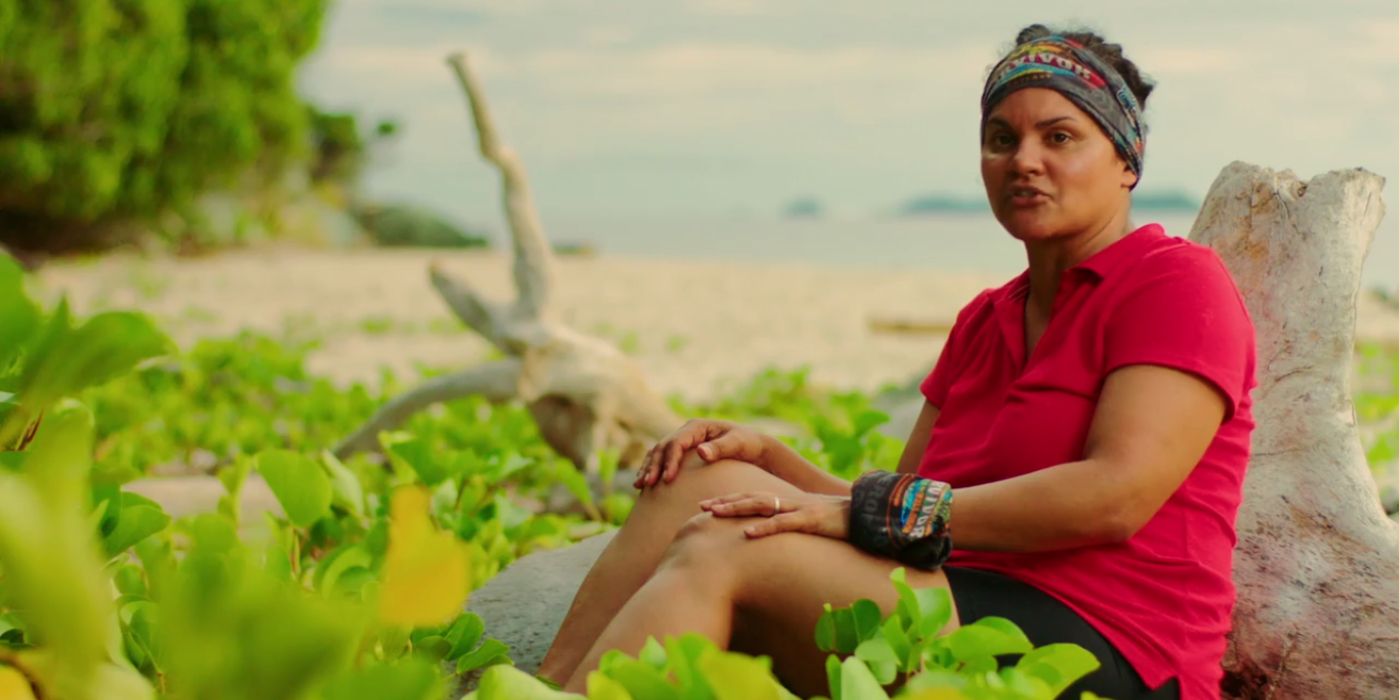 Sandra sitting against a stump in Survivor, talking to the camera.