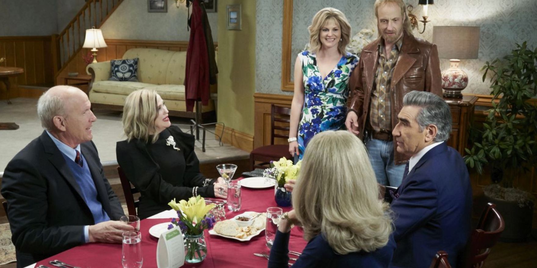 Roland and Jocelyn standing over a table of friends in Schitt&rsquo;s Creek