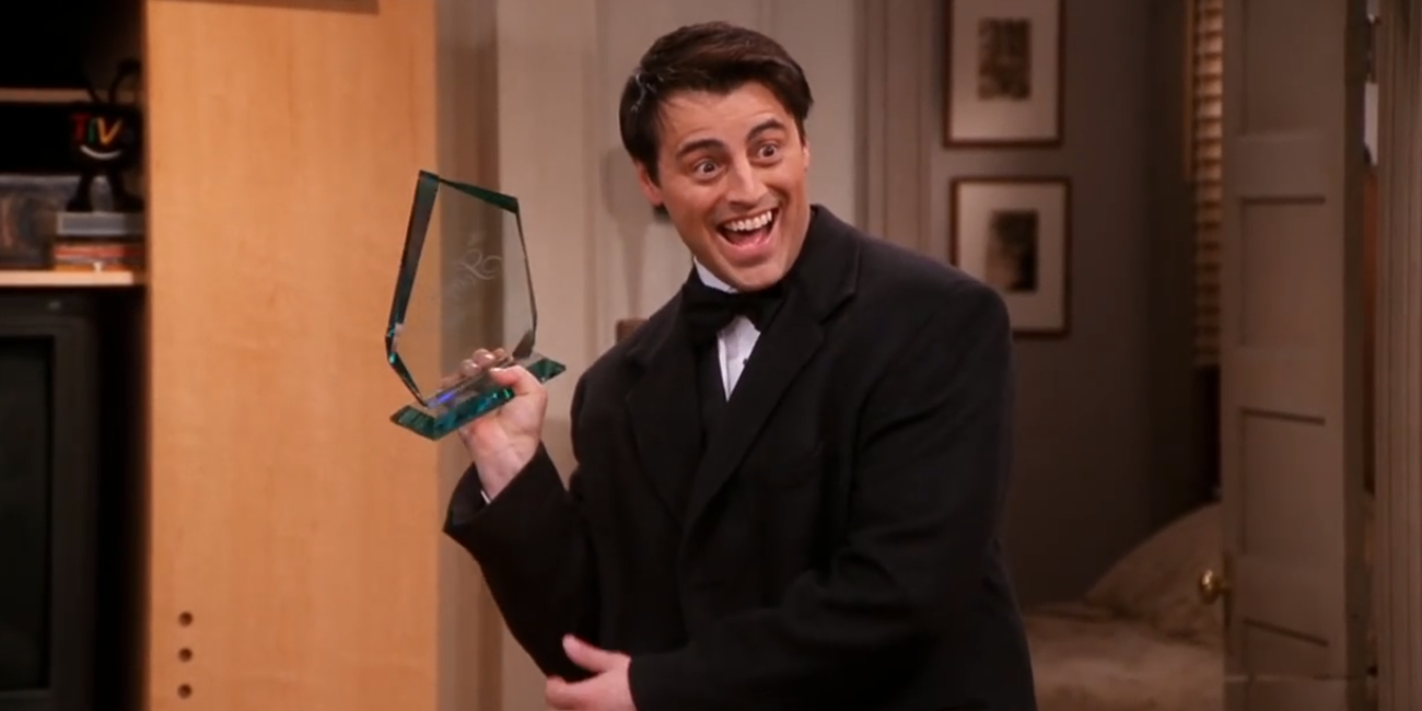 Joey segurando um prêmio e sorrindo em Friends.