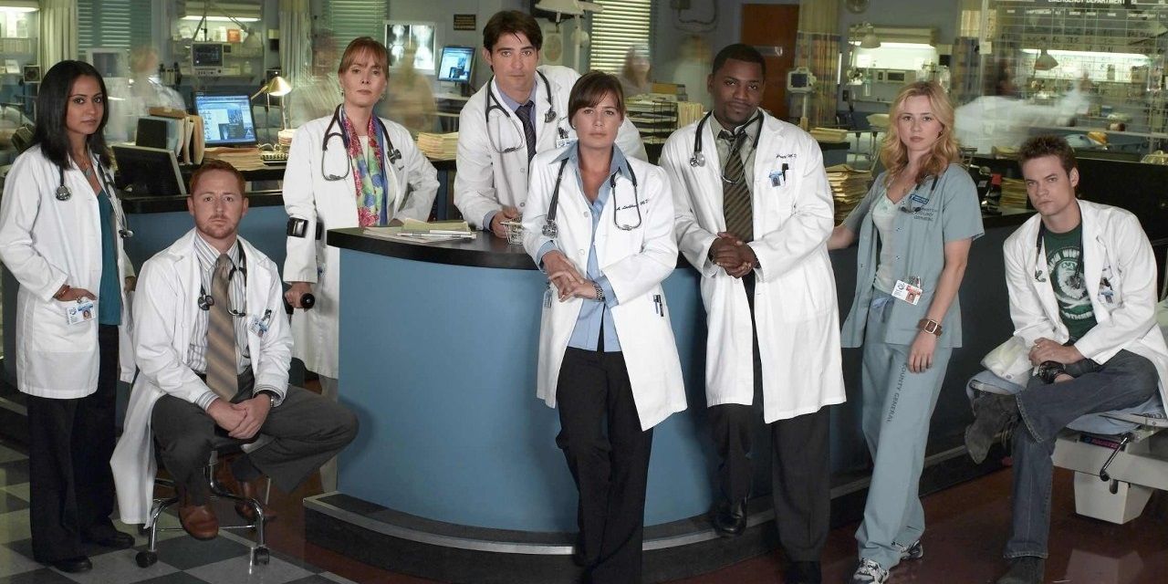 The cast of ER standing in front of a hospital reception desk.