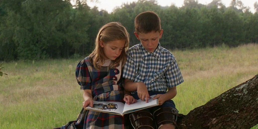 A jovem Jenny e Forrest Gump sentados em uma árvore lendo um livro ilustrado