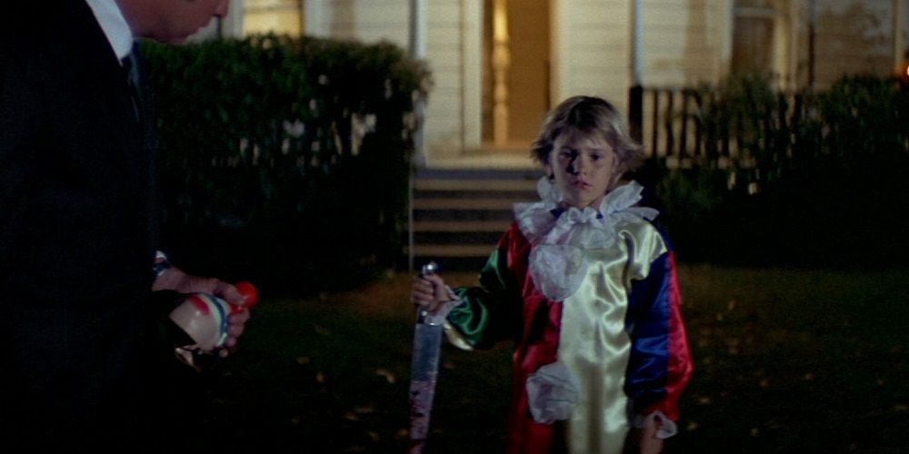 Young michael holding the knife outside his house as his father looks at him holding his clown mask at the beginning of the original Halloween