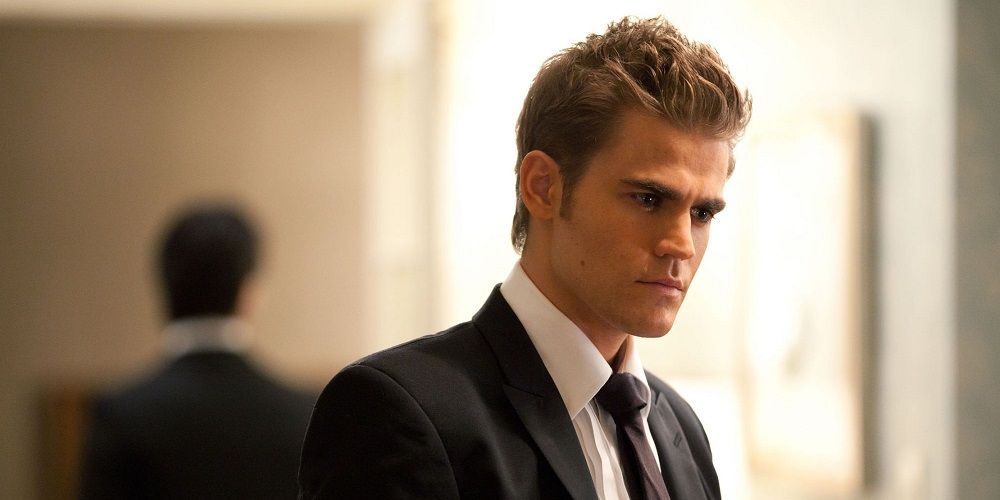 Stefan, in a black funeral suit, stares off to the side