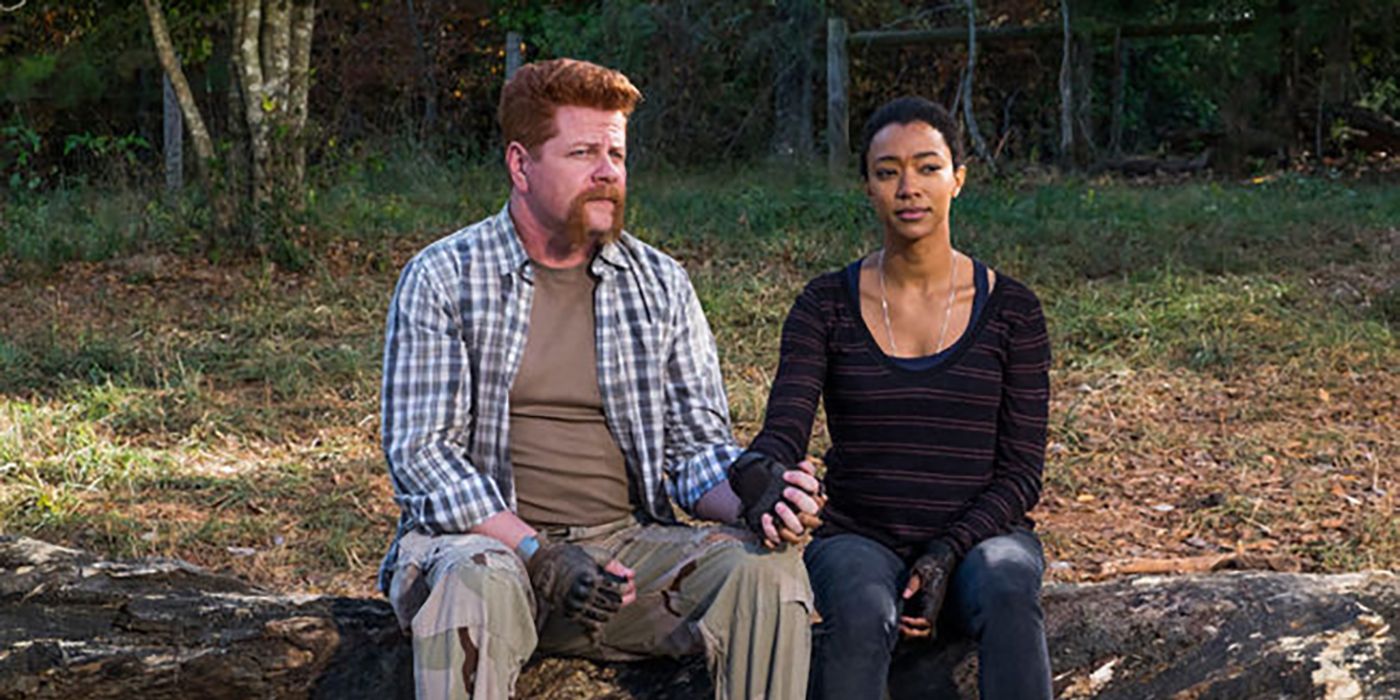 Sasha and Abraham holding hands and sitting on a fallen tree in The Walking Dead