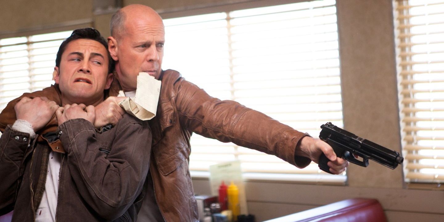 Bruce Willis with a gun holding Joseph Gordon-Levitt in Looper