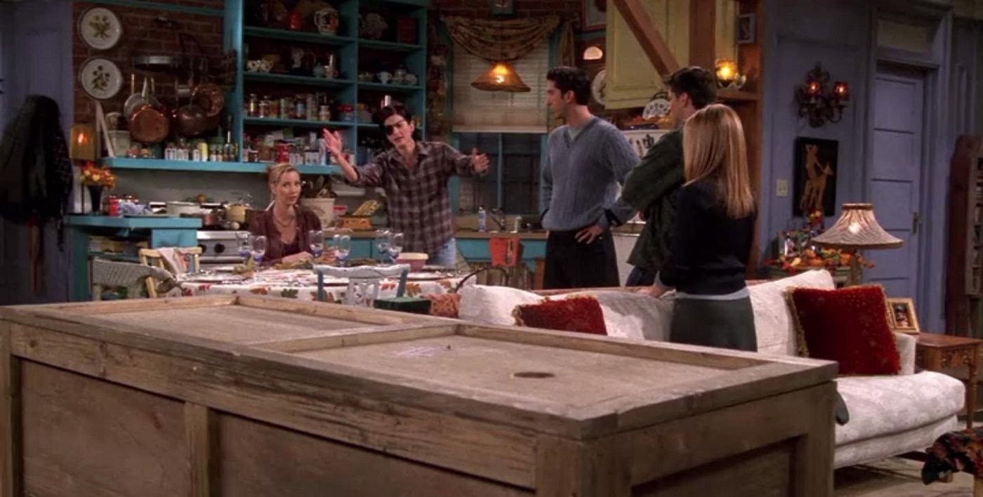 The friends sitting around the dinner table while Chandler lies in a wooden box