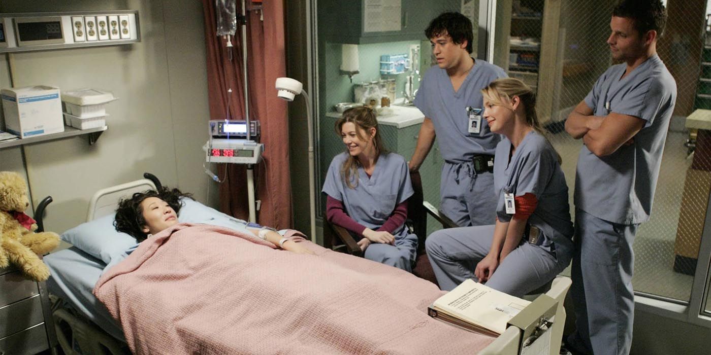 Cristina lies in a hospital bed as her intern friends hover around in Grey's Anatomy.