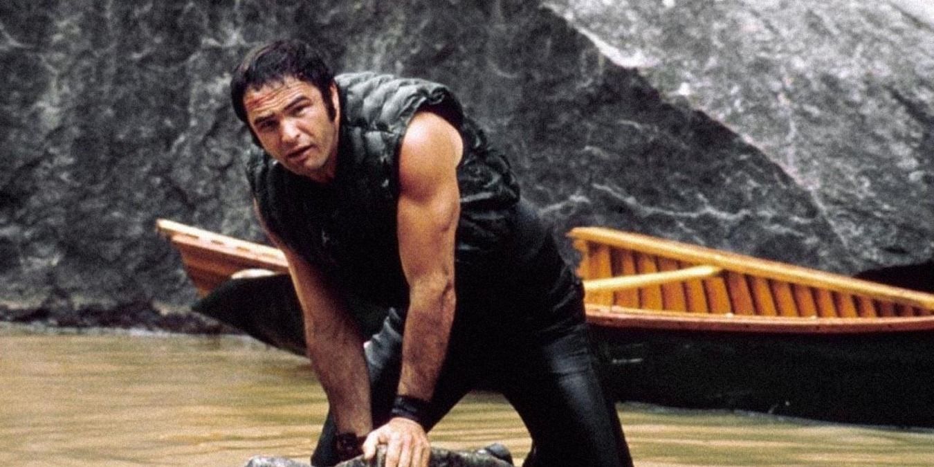Burt Reynolds standing in front of a canoe in water in Deliverance