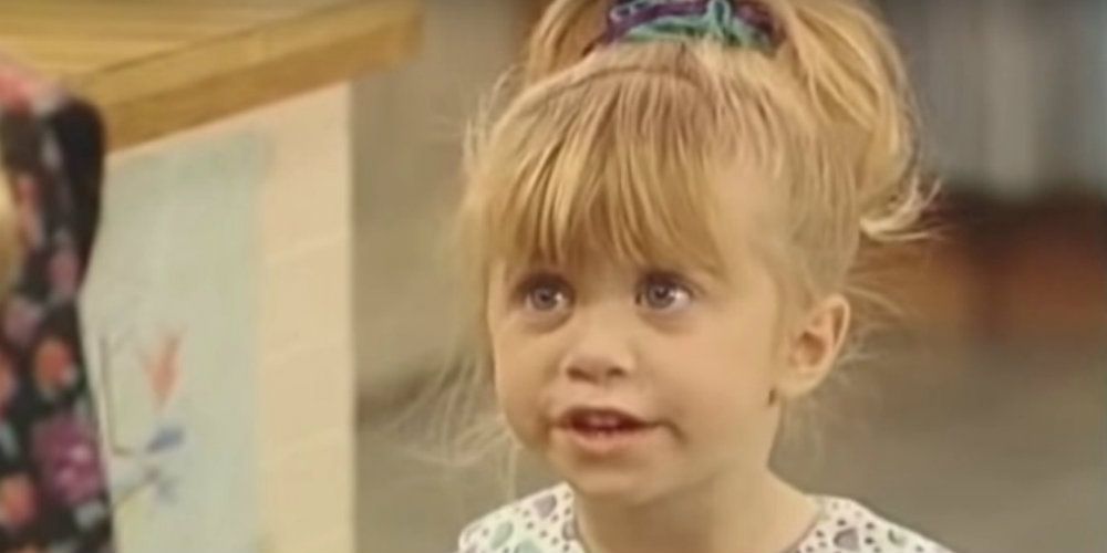 Michelle Tanner stands in the Tanner kitchen and looks mischievous