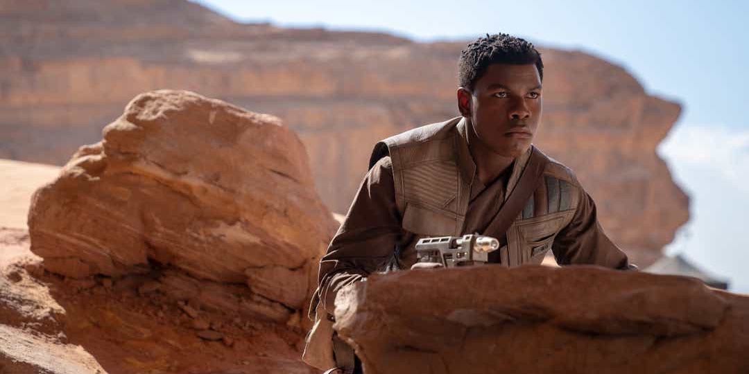 Finn holding a gun and hiding behind a rock, looking at the distance