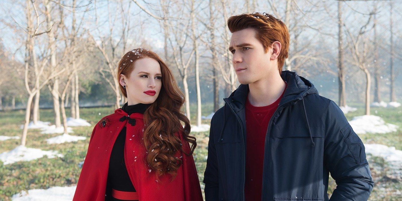 Cheryl Blossom in a black sweater and red cape staring at Archie who's wearing a red tee and a blue jacket on Riverdale