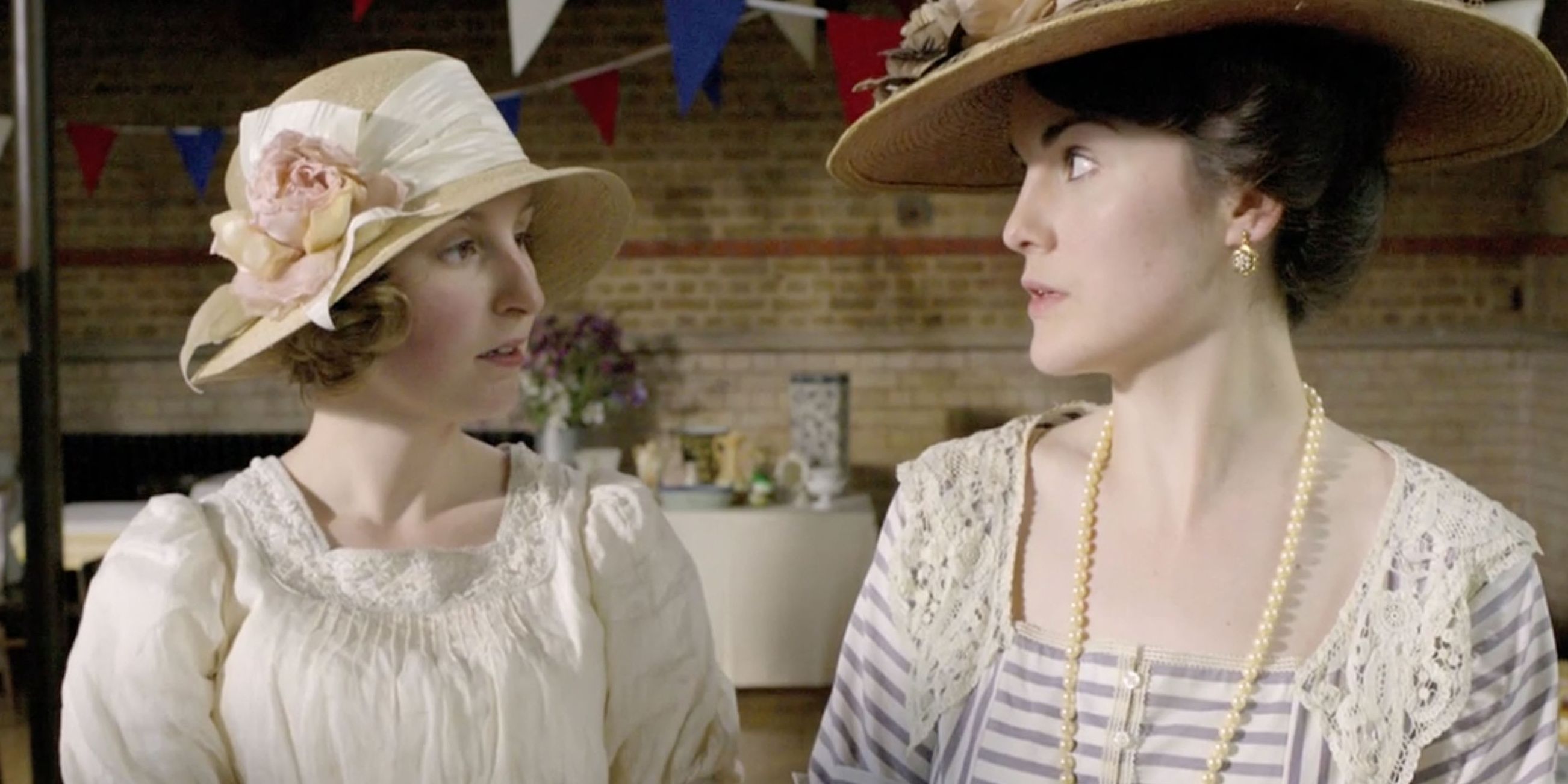 Mary and Edith look at each other while wearing hats in Downton Abbey.