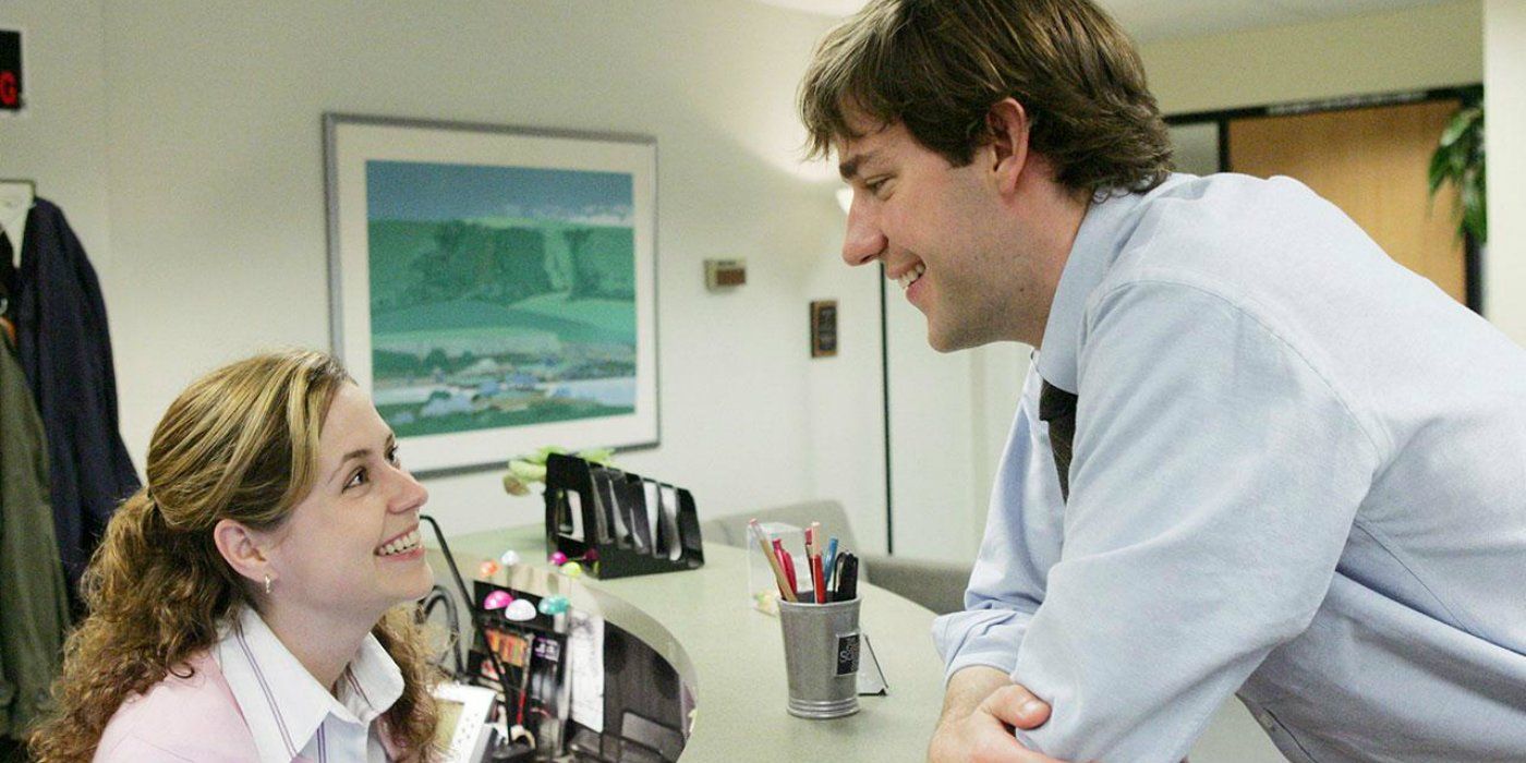 Pam smiles at Jim as he stands over her desk on The Office