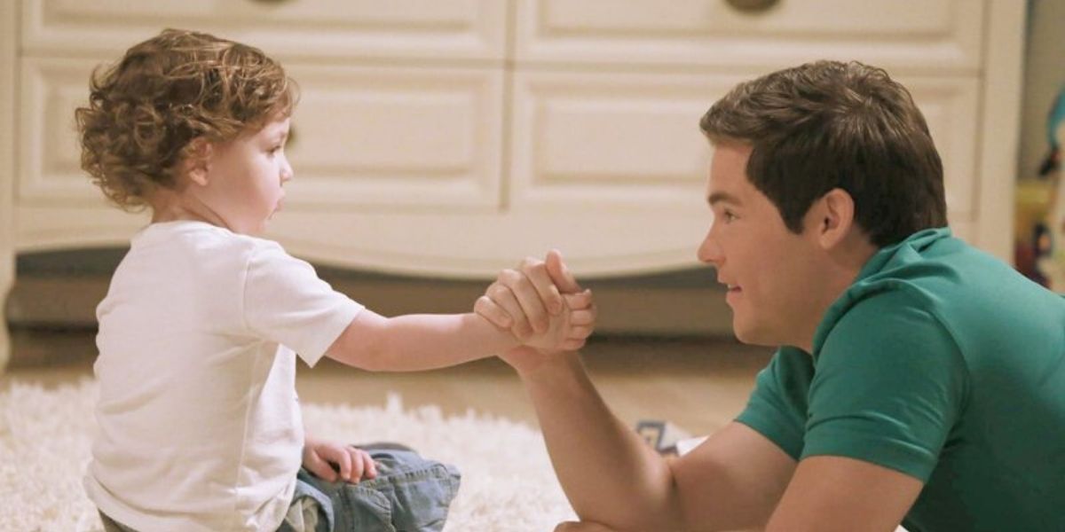 Andy holding hands with baby Joe in modern family