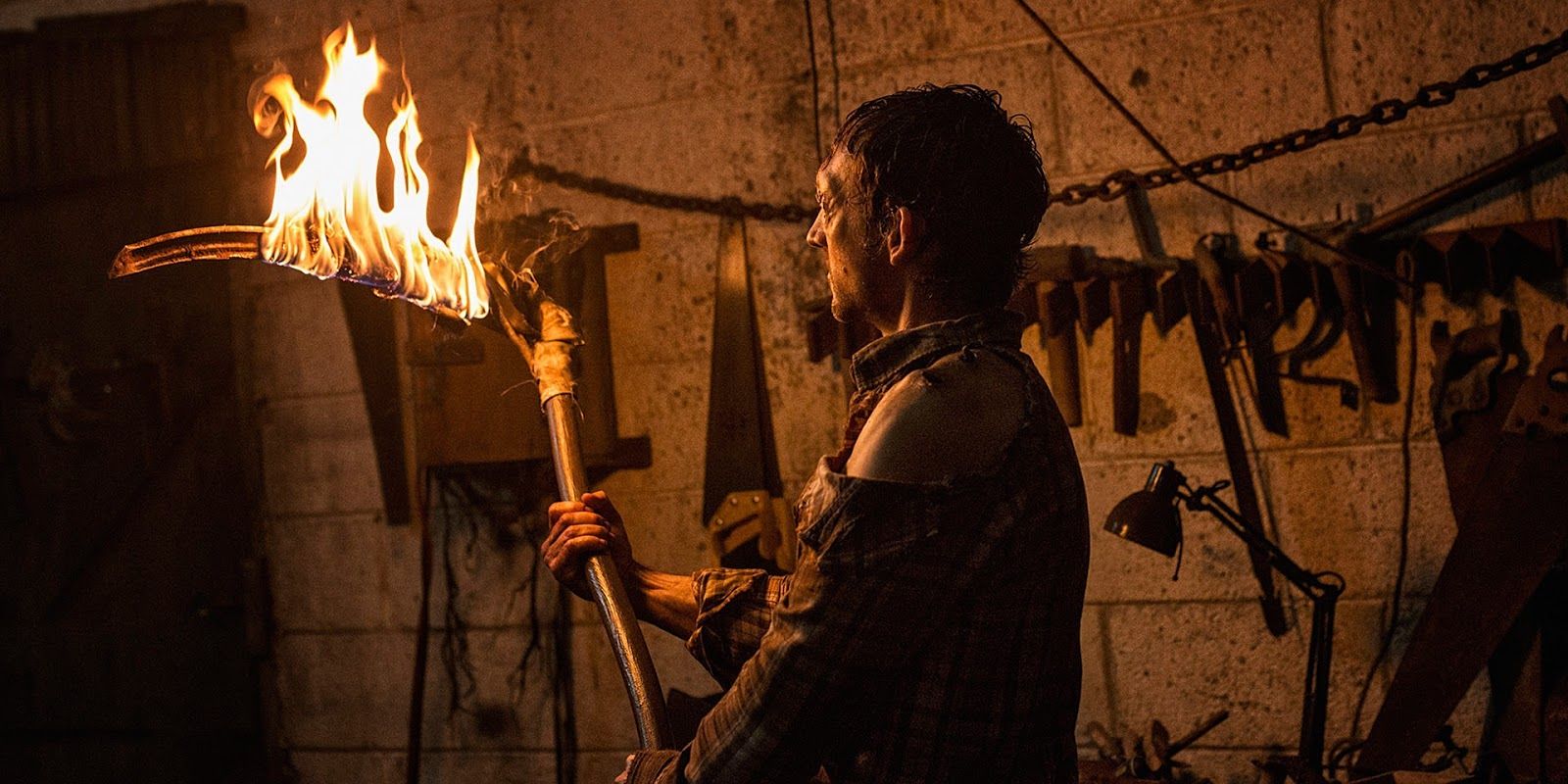 A man with a torch in a room of tools in The Hallow