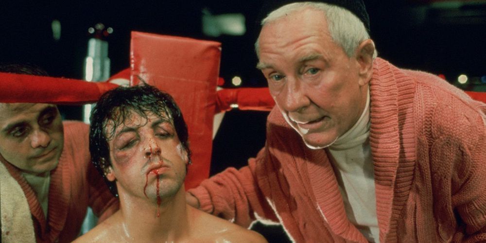 Mickey bendinng down next to a bloodied Rocky Balboa 