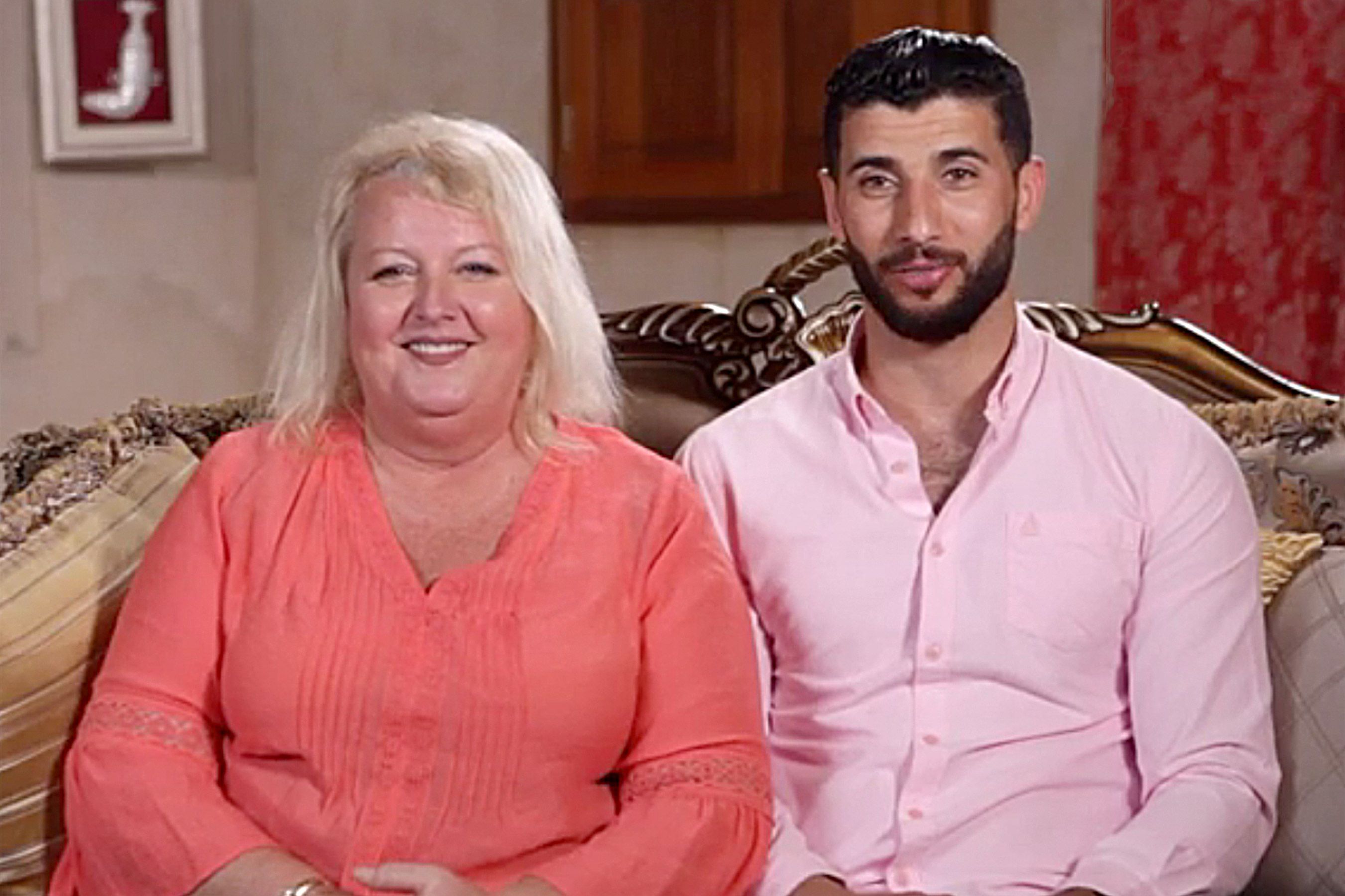 Lauren and Aladin sitting on a sofa smiling in 90 Day Fiance.