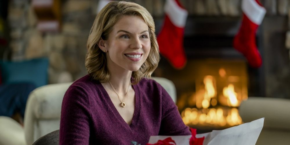 Ali Liebert smiling in front of a fireplace in Hallmark Christmas Movies